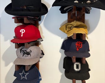 Puede incluir: Dos estantes de madera para sombreros que exhiben una variedad de sombreros. Los sombreros incluyen un fedora negro, una gorra de béisbol roja con una "P" blanca, una gorra gris con un bulldog y una gorra azul marino con una estrella blanca.