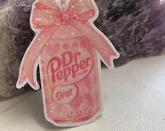May include: A pink Dr Pepper Diet can sticker with a bow and hearts design. The sticker features the text "Dr Pepper Est. 1885 Diet 12 OZ". The bow is glittery and the can has a heart pattern.
