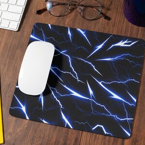 以下が含まれることがあります： 稲妻模様の黒と青の マウスパッド。白いコンピューターマウスがパッドの上に置かれています。