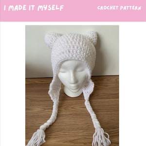 May include: A white crocheted Finn hat with ear flaps and braided ties with tassels. The hat is displayed on a mannequin head. The text "I MADE IT MYSELF" and "CROCHET PATTERN" are at the top. The text "FINN HAT" is at the bottom.