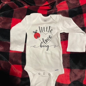 May include: White long-sleeve bodysuit with a black graphic that says "little love bug" with a red ladybug illustration.