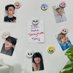 May include: A white refrigerator door with various magnets and photos. The magnets are cartoon animal faces and the photos are of a K-pop group. A handwritten note on a white piece of paper reads "You make Stray Kids Stay".