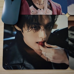 May include: A black mouse mat with a close-up image of a person eating a strawberry. The person is wearing a black leather jacket and a silver ring. A blue computer mouse is visible in the upper left corner.
