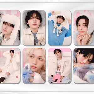May include: A set of eight photo cards featuring different members of a K-pop group. Each card has a white border and a pink background. The members are wearing various winter-themed outfits and accessories, including hats, scarves, and sweaters.