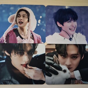 May include: Four square photo cards with images of young people. One card shows a person wearing a pink jacket and a furry hat. Another shows a person smiling. The third shows a person eating a strawberry. The last shows a person holding a white rabbit.