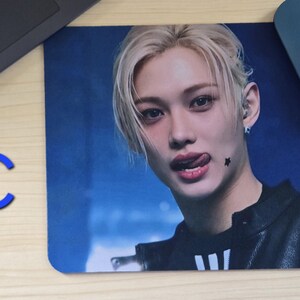 May include: Rectangular mousepad featuring a close-up of a person with blonde hair and a black jacket. The person is sticking out their tongue and has a star-shaped tattoo. A blue computer mouse is in the upper right corner.