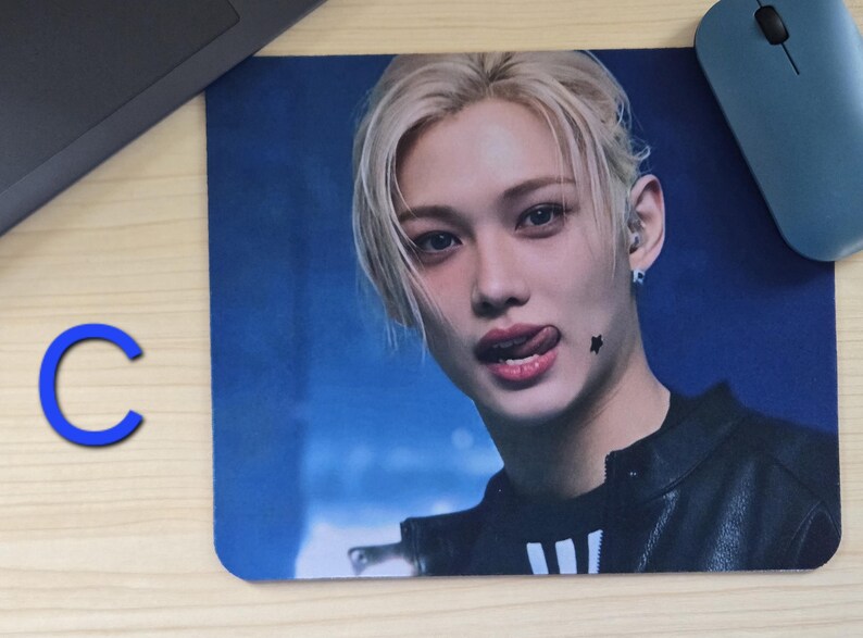 May include: Rectangular mousepad featuring a close-up of a person with blonde hair and a black jacket. The person is sticking out their tongue and has a star-shaped tattoo. A blue computer mouse is in the upper right corner.