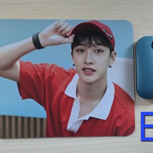 May include: A rectangular mousepad featuring a person wearing a red shirt and a red cap. A blue wireless mouse is next to the mousepad. A blue letter "B" is also in the image.