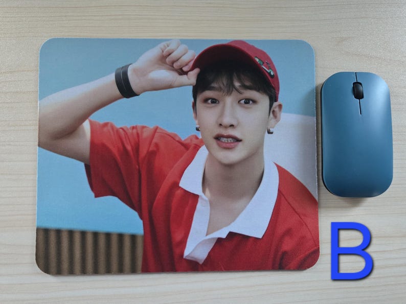 May include: A rectangular mousepad featuring a person wearing a red shirt and a red cap. A blue wireless mouse is next to the mousepad. A blue letter "B" is also in the image.