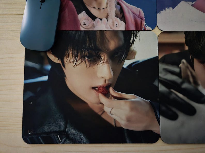 May include: A black mouse mat with a close-up image of a person eating a strawberry. The person is wearing a black leather jacket and a silver ring. A blue computer mouse is visible in the upper left corner.