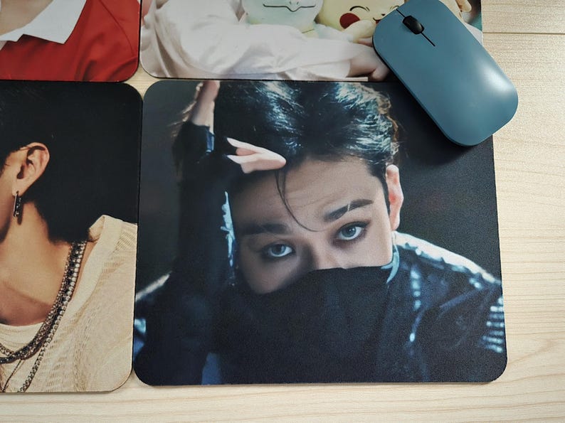 May include: A black mousepad featuring a close-up of a person with dark hair and striking blue eyes. The person's face is partially obscured by a black garment. A blue computer mouse rests on the surface.