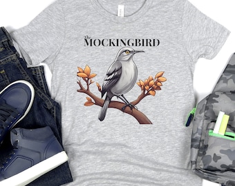 ¡La camisa del ruiseñor emplumó humor y estilo combinados! Perfecto para los entusiastas de las aves. Desata el ingenio aviar con nuestra camiseta gráfica Mockingbird.