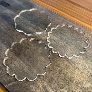 May include: Three clear acrylic scalloped circles of different sizes on a brown wooden surface.