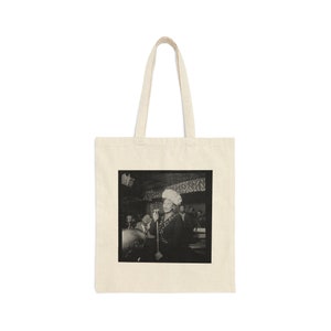 Puede incluir: Una foto en blanco y negro de una mujer cantando en un micrófono. Lleva un sombrero blanco y un vestido. La foto está impresa en una bolsa de tela.