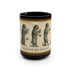 May include: A black coffee mug with a brown band around the middle. The band features a vintage illustration of a cat catching a ball of yarn. The text "EVOLUTION OF A CAT-CHER." is printed below the illustration.