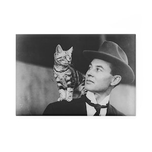 Puede incluir: Una fotografía en blanco y negro de un hombre con un sombrero y un gato sentado en su hombro.