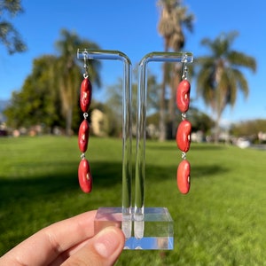 May include: A pair of dangle earrings featuring four red kidney beans on each earring, suspended from silver hooks.