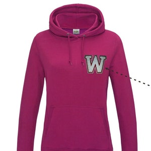Peut inclure: Un sweat à capuche magenta avec une capuche à cordon et une poche kangourou. Le sweat à capuche présente un grand écusson "W" bordé d'argent sur la poitrine. Le sweat-shirt à manches longues est en matière douce.