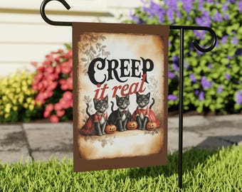 May include: A Halloween garden flag with a brown border features three black cats dressed in costumes, each holding a pumpkin. The flag reads "Creep it real" in a vintage font, perfect for spooky season.