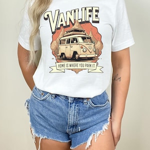 May include: White t-shirt with a graphic of a vintage camper van with the text "VANLIFE" and "HOME IS WHERE YOU PARK IT" printed on it.