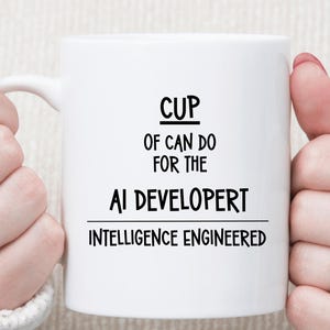 May include: White ceramic mug with the text "CUP OF CAN DO FOR THE AI DEVELOPERT INTELLIGENCE ENGINEERED" in black. The mug is held by two hands, with rings on the fingers.