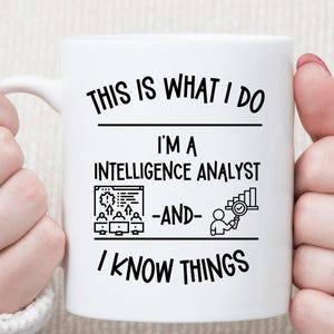 May include: A white ceramic mug featuring black text that reads: THIS IS WHAT I DO I'M A INTELLIGENCE ANALYST -AND- I KNOW THINGS. The design includes a graphic of people at computer stations and a person looking at a bar chart with a magnifying glass.