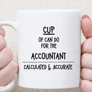 May include: White ceramic mug with the text "CUP OF CAN DO FOR THE ACCOUNTANT CALCULATED & ACCURATE" in black. The mug is held by two hands, with rings on the fingers. The mug is a standard size for coffee or tea.