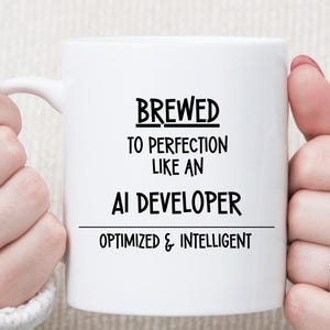 May include: White ceramic mug with the text "BREWED TO PERFECTION LIKE AN AI DEVELOPER OPTIMIZED & INTELLIGENT" in black. The mug is held by two hands, with rings on the fingers.