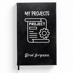May include: Black leather journal with the text "MY PROJECTS" and a white icon of a scroll with the word "PROJECT" and a gear. The journal is personalised with the name "Brad Jorgensen".