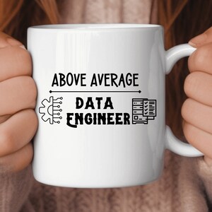 May include: White ceramic mug with black text that reads "Above Average Data Engineer". The text is surrounded by a small graphic of a computer chip and a server.