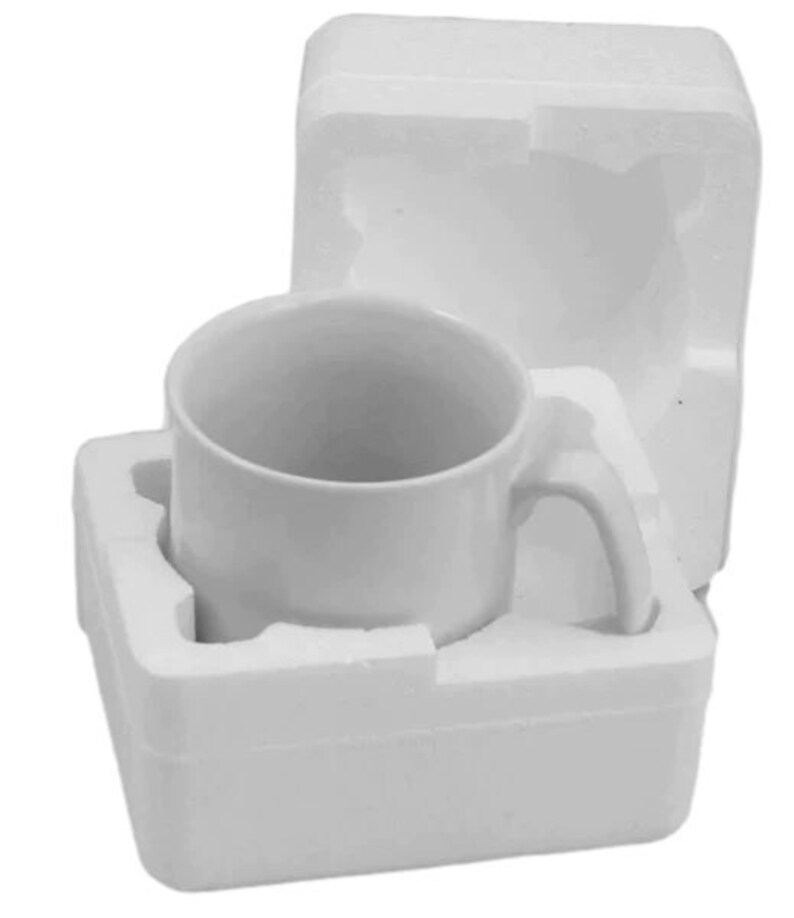 K&ouml;nnte beinhalten: Eine wei&szlig;e Keramiktasse mit gebogenem Henkel, verpackt in wei&szlig;em Schaumstoff. Die Tasse ist zylindrisch und leer. Die Verpackung dient zum Schutz der Tasse w&auml;hrend des Transports und der Lagerung.