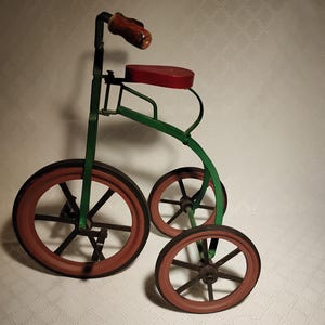 May include: A vintage-style tricycle with a green frame, red seat, and wheels. The handlebars are brown, and the wheels have a red rim. This classic toy is a charming decorative piece.