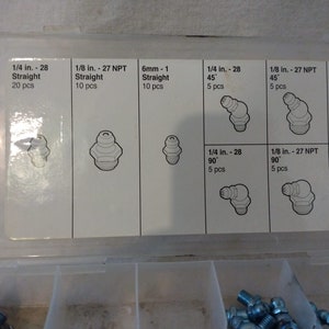 Op de afbeelding: Een transparante kunststof opbergdoos met een wit label. Het label toont een verscheidenheid aan verschillende maten en stijlen van smeernippels. Het label bevat de volgende tekst: 1/4 in. - 28 Straight 20 pcs, 1/8 in. - 27 NPT Straight 10 pcs, 6mm - 1 Straight 10 pcs, 1/4 in. - 28 45 5 pcs, 1/8 in. - 27 NPT 45 5 pcs, 8mm - 1 Straight 5 pcs, 1/4 in. - 28 90&deg; 5 pcs, 1/8 in. - 27 NPT 90 5 pcs, 10mm - 1 Straight 5 pcs.