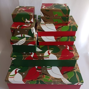 May include: A stack of decorative gift boxes in various sizes. The boxes feature a festive design with red, green, and white birds, leaves, and berries on a brown background. The box bases are red and green.