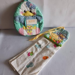 May include: A set of kitchen accessories featuring a duck theme. Includes a quilted egg-shaped pot holder with a pocket labeled "NOTES", a matching oven mitt, and a white towel with colorful egg and dot patterns.