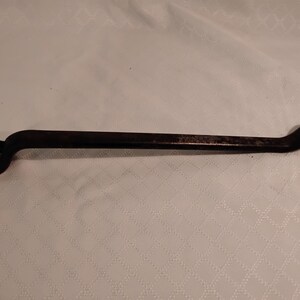 May include: A vintage, dark brown wrench with a closed-end and open-end design. The tool is made of metal and shows signs of wear, suggesting it's been used. The wrench is designed for tightening or loosening nuts and bolts.