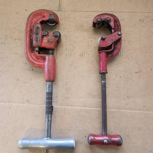 K&ouml;nnte beinhalten: Zwei rote Rohrschneider mit silbernen Griffen. Der Schneider links tr&auml;gt die Aufschrift "RIDGID". Der Schneider rechts tr&auml;gt die Aufschrift "BAUMDER".