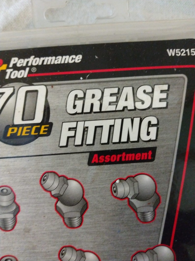 Op de afbeelding: Een verpakking met 70 stuks smeernippel assortiment. De verpakking is zwart met rode en witte tekst. De tekst op de verpakking luidt "Performance Tool" en "70 Piece Grease Fitting Assortment". De verpakking toont een close-up van verschillende smeernippels.
