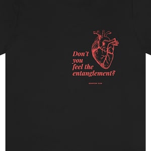 Peut inclure: T-shirt noir avec une illustration rouge d'un cœur anatomique et le texte "Don't you feel the entanglement?" imprimé sur le devant.