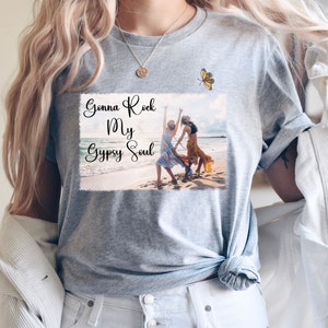 K&ouml;nnte beinhalten: Graues T-Shirt mit einem Motiv von zwei Frauen, die am Strand tanzen, mit dem Text "Gonna Rock My Gypsy Soul" und einem Schmetterling &uuml;ber dem Motiv.