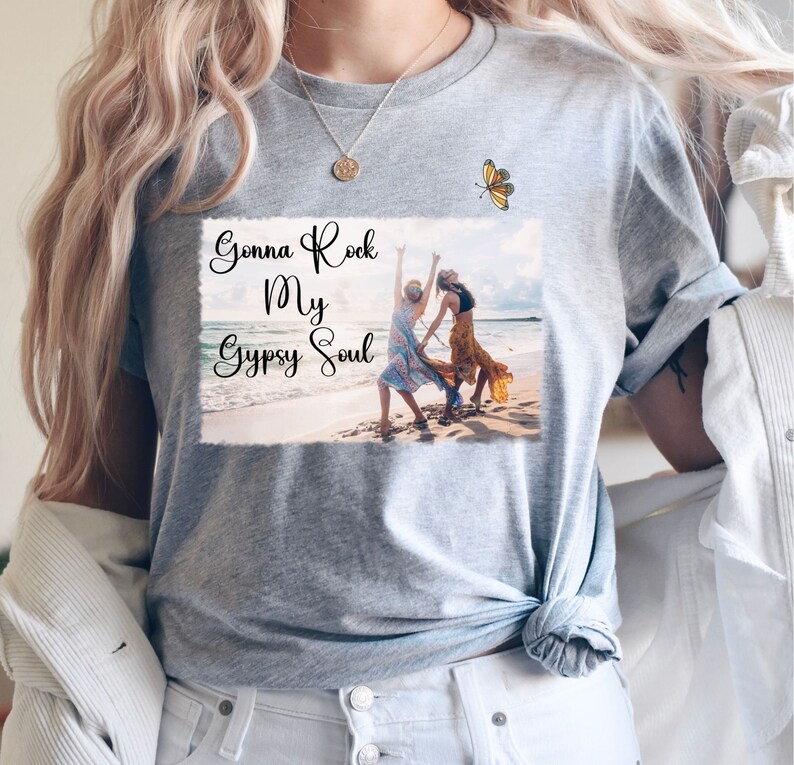 K&ouml;nnte beinhalten: Graues T-Shirt mit einem Motiv von zwei Frauen, die am Strand tanzen, mit dem Text "Gonna Rock My Gypsy Soul" und einem Schmetterling &uuml;ber dem Motiv.