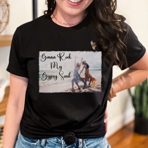 K&ouml;nnte beinhalten: Schwarzes T-Shirt mit einer wei&szlig;en Grafik von zwei Frauen, die am Strand tanzen, mit dem Text "Gonna Rock My Gypsy Soul" in einer verwitterten Schrift.