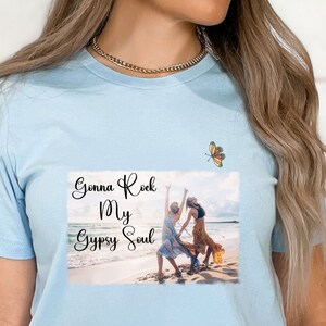 K&ouml;nnte beinhalten: Hellblaues T-Shirt mit einem Foto von zwei Personen am Strand und dem Text "Gonna Rock My Gypsy Soul". Oben rechts befindet sich eine kleine Schmetterlingsgrafik.