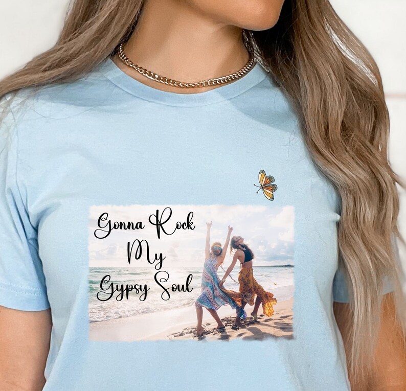 K&ouml;nnte beinhalten: Hellblaues T-Shirt mit einem Foto von zwei Personen am Strand und dem Text "Gonna Rock My Gypsy Soul". Oben rechts befindet sich eine kleine Schmetterlingsgrafik.
