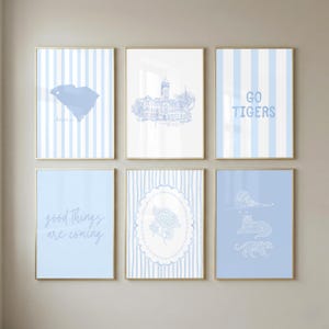 May include: A set of six wall art prints featuring light blue and white color schemes. Designs include a map of South Carolina, a building illustration, the text GO TIGERS, the text good things are coming, a floral oval frame, and three tigers.