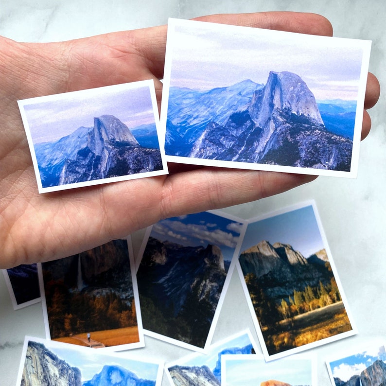 May include: A collection of eight photographs of Yosemite National Park, featuring various views of Half Dome, a granite dome in the park. The photos are printed on white cardstock and are arranged in a hand.