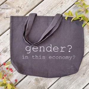 Könnte beinhalten: Eine schwarze Tragetasche mit weißem Text, der "gender? in this economy?" lautet.