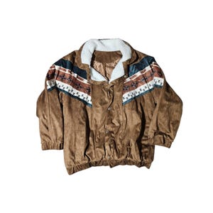 May include: Brown suede jacket with a white faux fur collar and a geometric pattern across the shoulders. The jacket has a button-up front and elastic cuffs. The pattern includes white, brown, and teal geometric shapes.