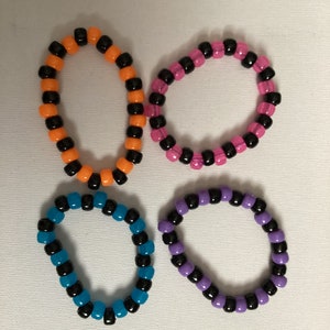 May include: Four colorful friendship bracelets with black beads. The bracelets are made with orange, pink, blue, and purple beads.