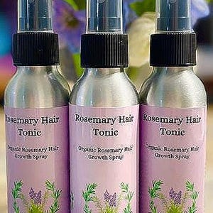 Puede incluir: Tres botellas de spray plateadas de Rosemary Hair Tonic con tapas negras y etiquetas rosas. Las etiquetas presentan el texto "Rosemary Hair Tonic" y "Organic Rosemary Hair Growth Spray" con una ilustraci&oacute;n floral. Las botellas son de 118 ml.